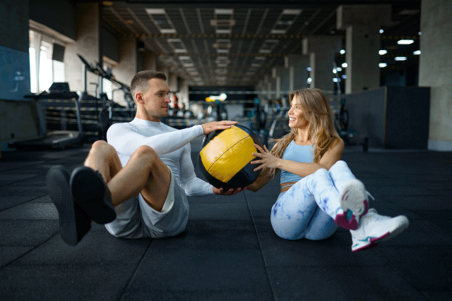 pareja entrenando en un gimnasio con un balón medicinal